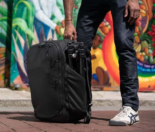 a person holding a black Peak Design Travel Backpack