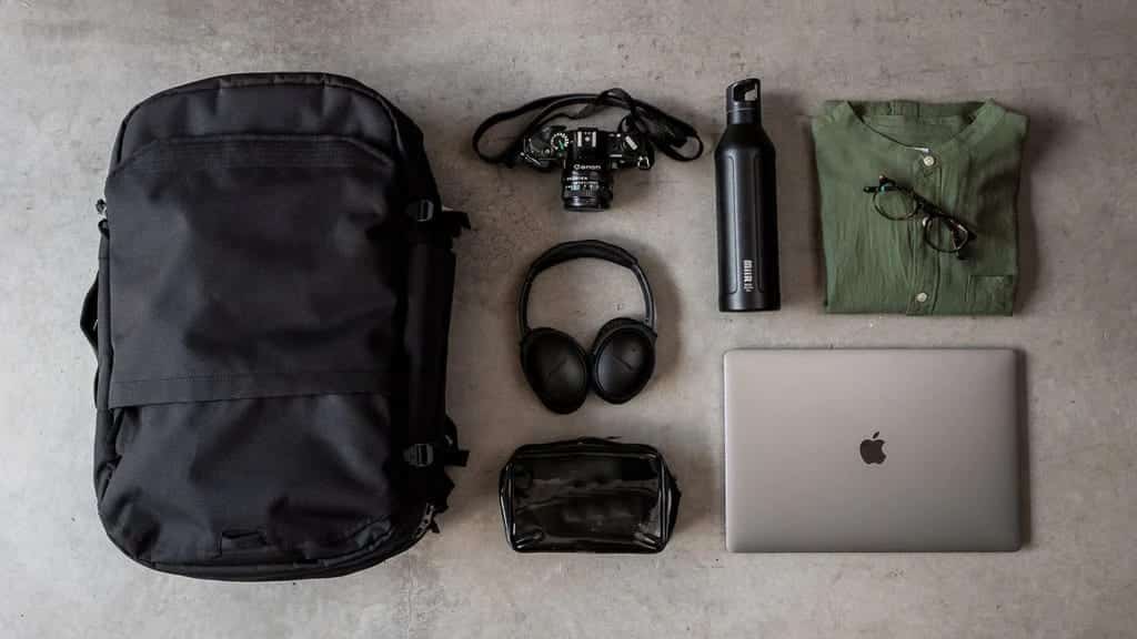 a backpack placed on a smooth surface with accessories such as headphones waterbottle laptop and pouch