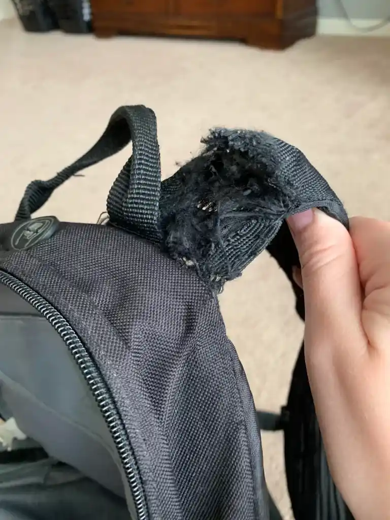 a person holding a damaged backpack strap with his hand 