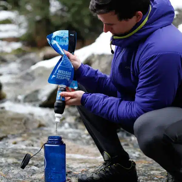 a man pouring clean water in a bottle using Sawyer Squeeze Water Filter System