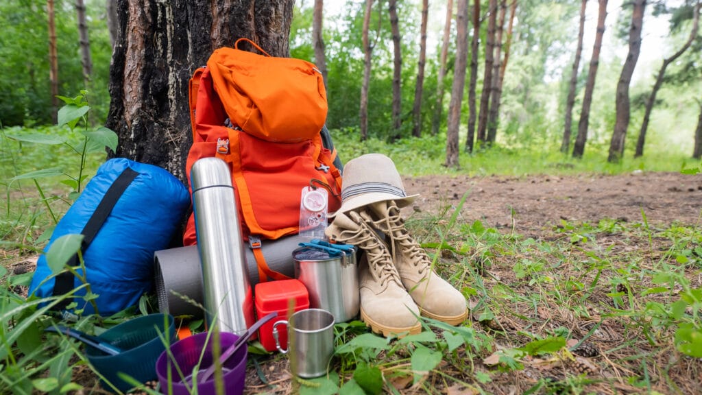 Hiking equipment in a pine forest Backpack thermos sleeping bag compass hat and shoes