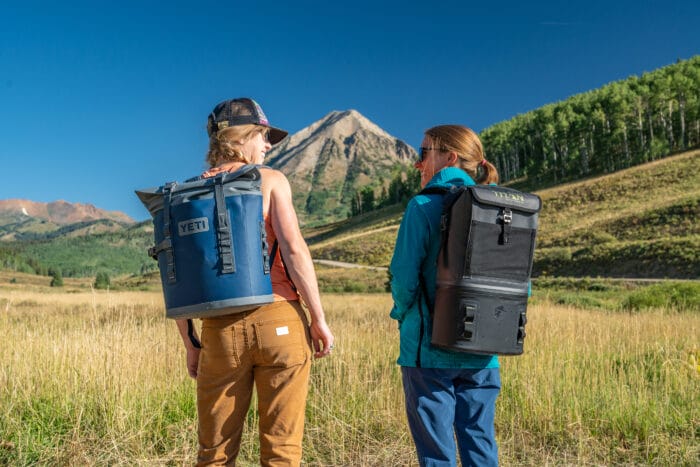 two travellers carrying their backpack coolers