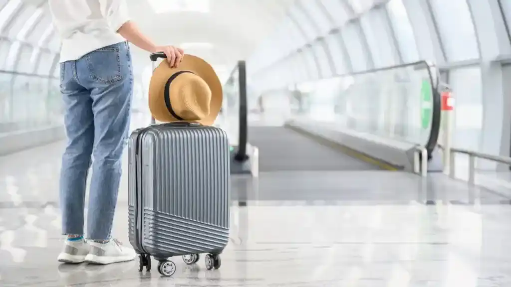 a man standing with his carry on luggage and a hat in hand