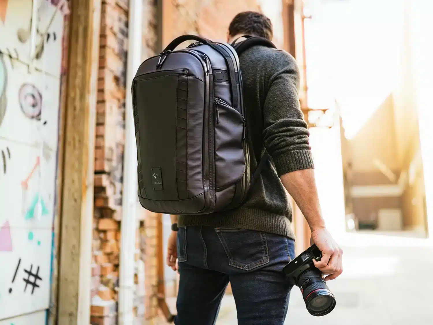 a man wearing a Nomatic McKinnon Camera Pack L on back with a camera in one hand