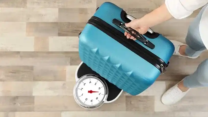 a man weighing his carry on luggage on a weight machine