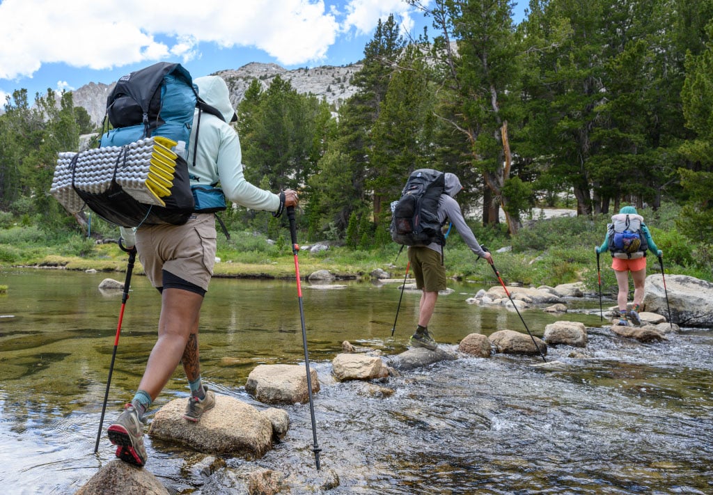 three hikers walking on the stones inside the flowing water