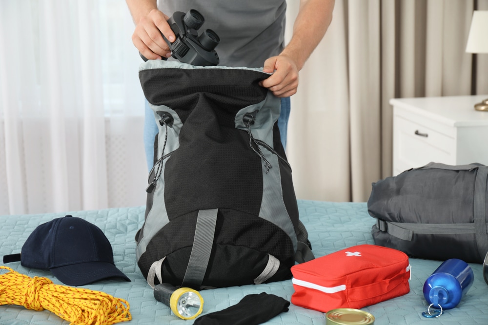 Man Packing Different Camping Equipment Into Backpack At Home Closeup