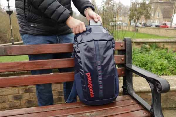 a man placing his phone in Patagonia Black Hole Pack L  placed on a bench