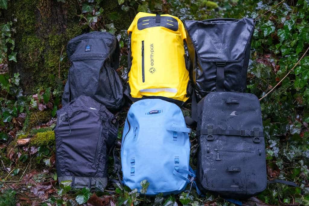 different ypes of waterproof backpacks lying on the ground in the forest