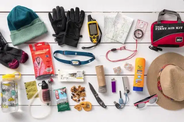 Assorted hiking essentials laid out including gloves first aid kit map snacks and water bottle Assorted hiking essentials laid out including gloves first aid kit map snacks and water bottle