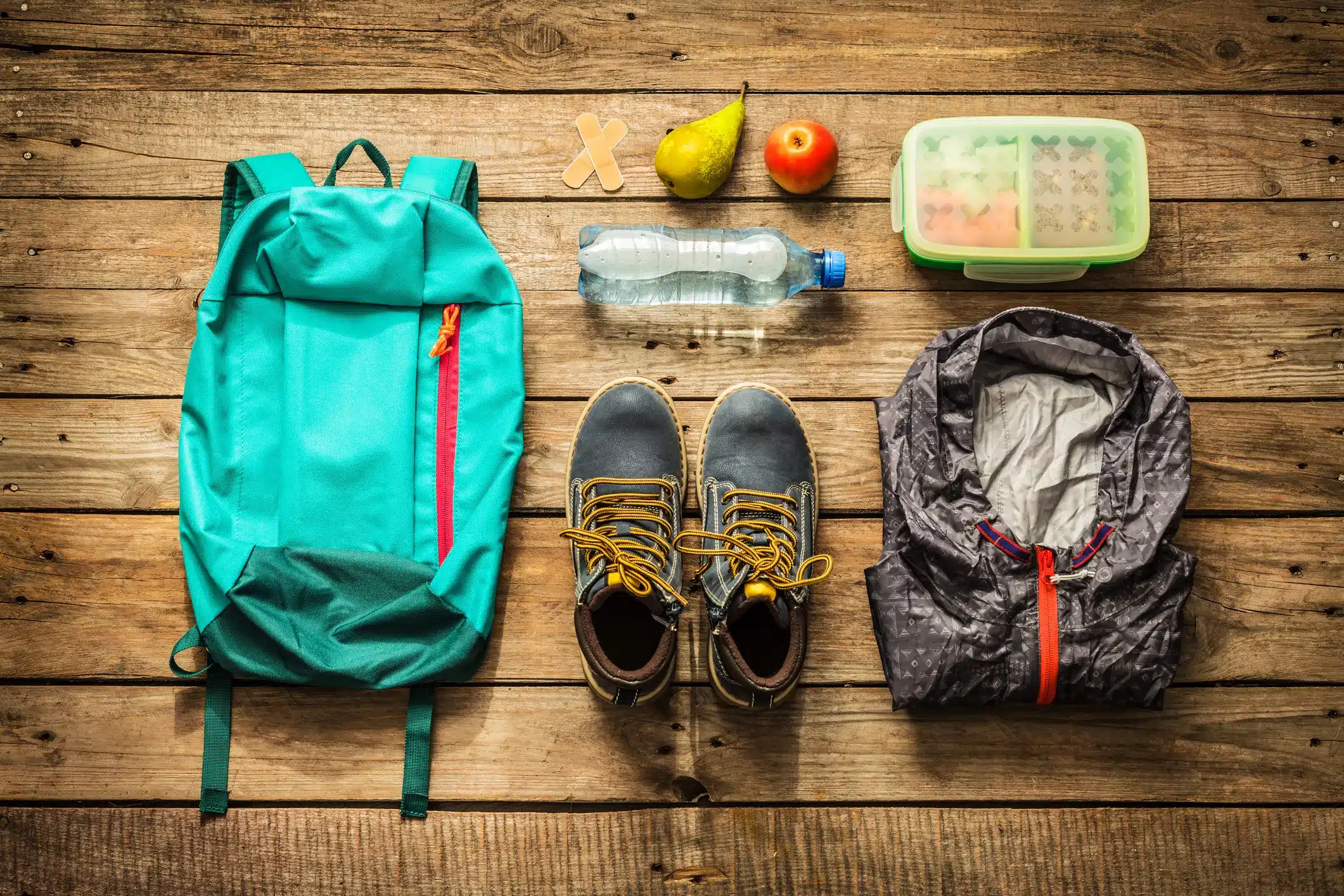 Essential hiking gear laid out including a daypack boots water bottle fruits and a jacket Essential hiking gear laid out including a daypack boots water bottle fruits and a jacket