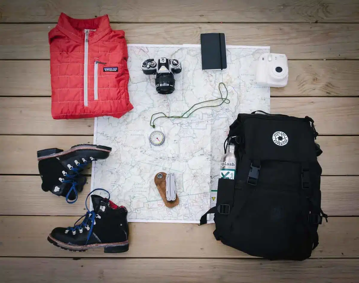 Hiking essentials laid out including a jacket boots camera map backpack water bottle and compass Hiking essentials laid out including a jacket boots camera map backpack water bottle and compass